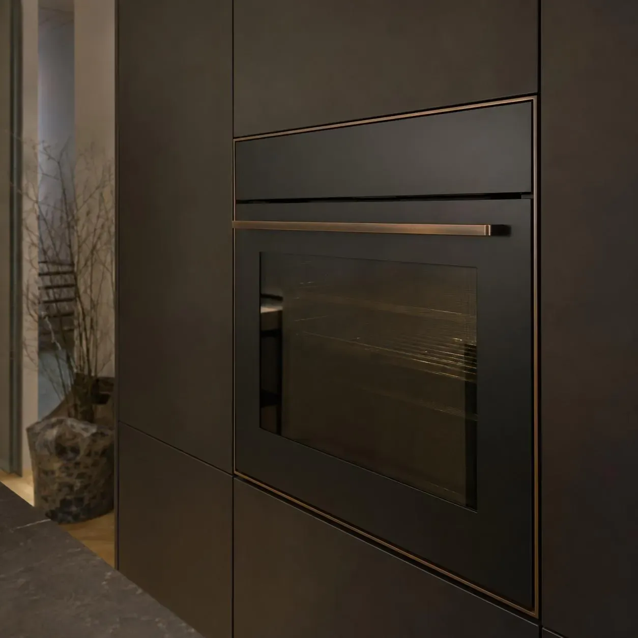 Matte-black built-in wall oven with bronze trim in dark cabinetry